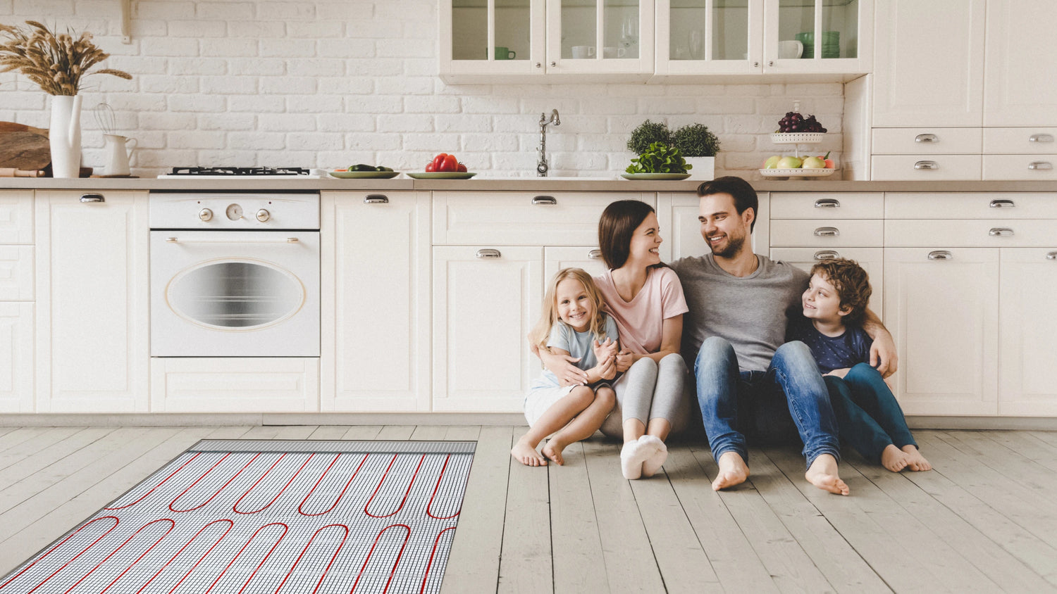 Happy family sitting comfortably on warm vinyl plank kitchen floor with electric underfloor heating cables visible, demonstrating family-friendly heated LVP flooring comfort.