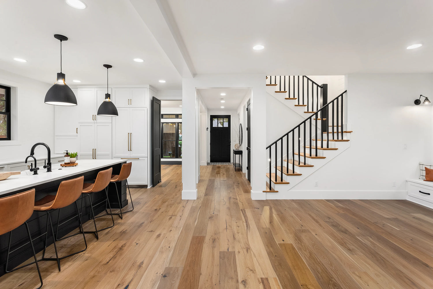 Open-concept kitchen and hallway featuring wide plank heated hardwood floors and modern black accents.
