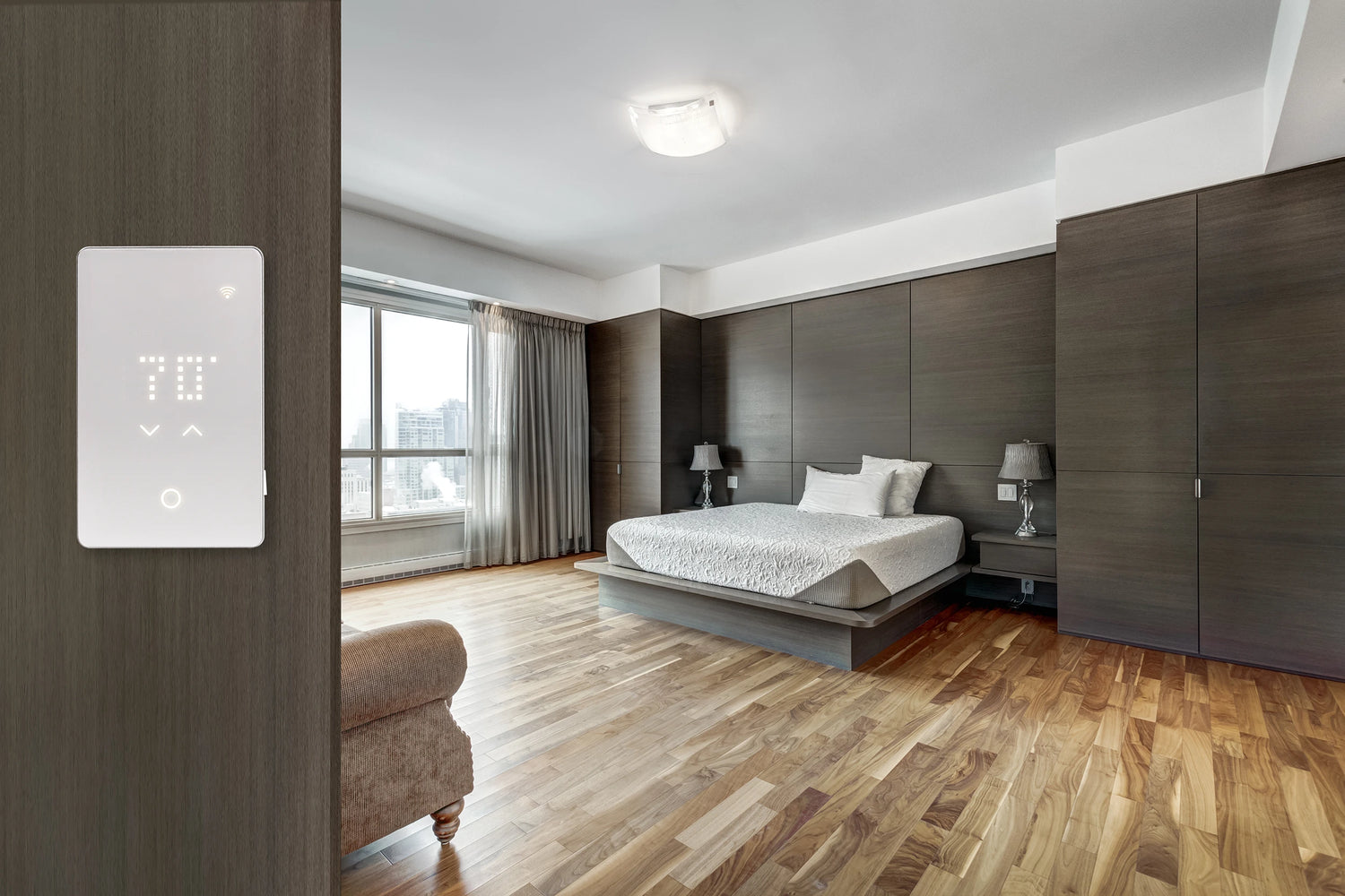 Modern bedroom with hardwood floor and smart thermostat on the wall for radiant floor heating.